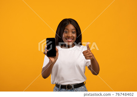 Smiling black lady showing mobile phone with empty screen 76748402