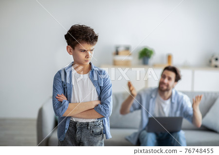 Furious father shouting at offended son while sitting with laptop computer on sofa at home, selective focus 76748455