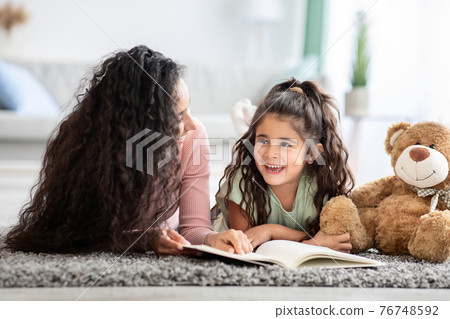 Loving young mother and her cute little daughter reading book at home 76748592