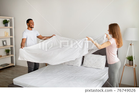 Cheerful multiracial couple making bed in morning, having fun at home Cheerful multiracial couple making bed in morning, having fun at home 76749026