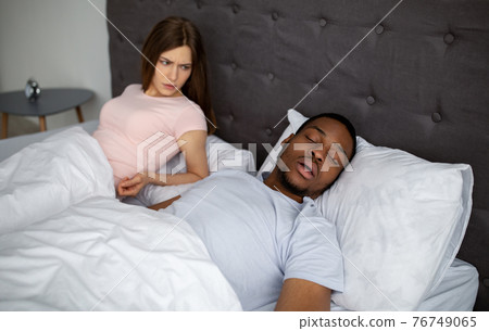 Young black guy snoring and bothering his angry sleepless wife in bed at home 76749065