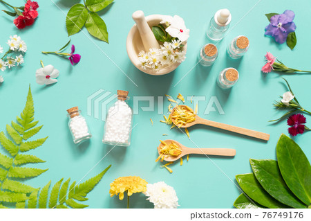 Homeopathic globules bottle with herb, flower, spoon and motar on green backgound. Homeopathy alternative medicine concept. Top view. 76749176