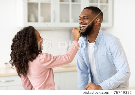 African American daughter cooking fresh salad feeding dad 76749355