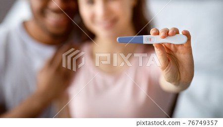 We gonna be parents. Happy multiracial couple in love showing positive pregnancy test on camera, selective focus 76749357