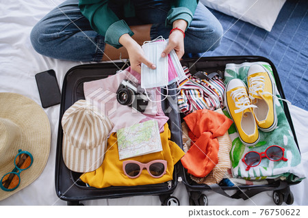 Unrecognizable woman with suitcase packing for holiday at home, coronavirus concept. 76750622