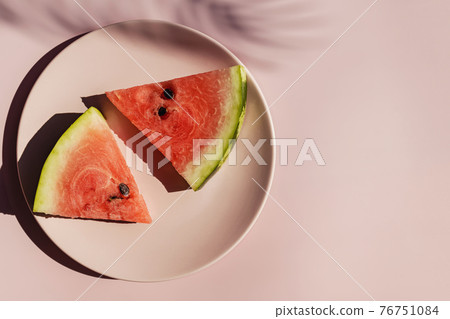 Fresh red watermelon slices on pink plate and tropical leaf shadow. Fresh red watermelon slices on pink plate and tropical leaf shadow. 76751084
