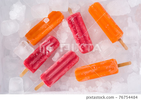 Orange and strawberry popsicles on ice cubes. Orange and strawberry popsicles on ice cubes. 76754484