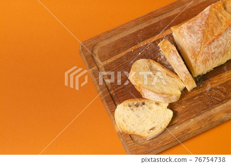 Sliced bread baguette on a wooden cutting board on a terracote color background. Close-up high quality photo. Sliced bread baguette on a wooden cutting board on a terracote color background. Close-up high quality photo. 76754738