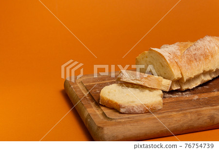 Sliced bread baguette on a wooden cutting board on a terracote color background. Close-up high quality photo. Sliced bread baguette on a wooden cutting board on a terracote color background. Close-up high quality photo. 76754739
