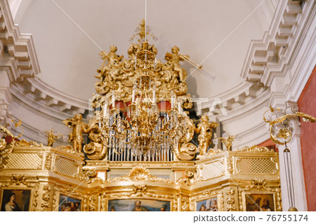 Large golden chandelier with candles in the church against the background of the organ. 76755174