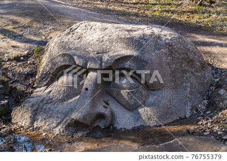 Russia. April 18, 2021. Sculpture of a knight's head sticking out of the ground in the Sergievka Park of the Lomonosovsky district of St. Petersburg. 76755379