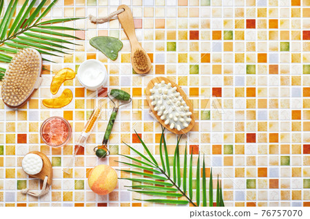 Jars of cream and gel for face and body care, gold eye patches and serum with gold, jade roller massager gau-sha and massager and body brush against background of tile mosaic 76757070