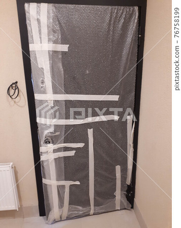 The new iron door is sealed with tape and foil to protect it from damage during repairs in a new building The new iron door is sealed with tape and foil to protect it from damage during repairs in a new building 76758199