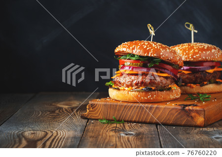 Two delicious homemade burgers of beef, cheese and vegetables on an old wooden table. Fat unhealthy food close-up. With copy space Two delicious homemade burgers of beef, cheese and vegetables on an old wooden table. Fat unhealthy food close-up. With copy space 76760220
