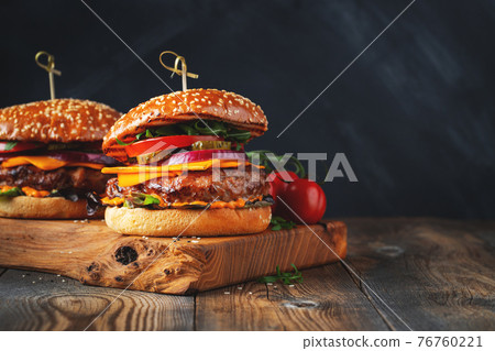 Two delicious homemade burgers of beef, cheese and vegetables on an old wooden table. Fat unhealthy food close-up. With copy space Two delicious homemade burgers of beef, cheese and vegetables on an old wooden table. Fat unhealthy food close-up. With copy space 76760221