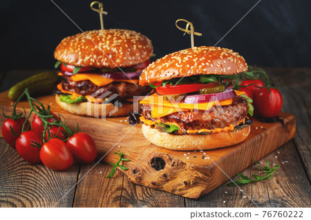Two delicious homemade burgers of beef, cheese and vegetables on an old wooden table. Fat unhealthy food close-up Two delicious homemade burgers of beef, cheese and vegetables on an old wooden table. Fat unhealthy food close-up 76760222