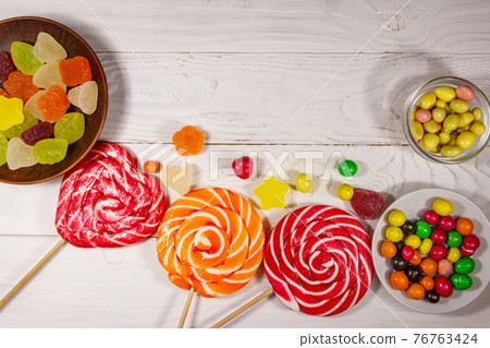 Colorful chocolate candies, lollipops and jelly sweets on white wooden table 76763424