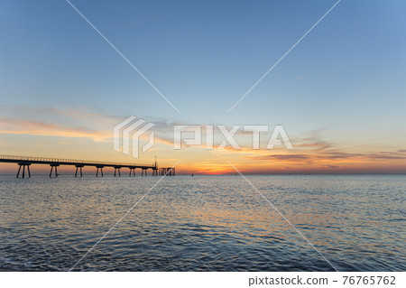 Early morning a few minutes before sunrise. Dawn on the sea with pontoon. Blue sky is painted in shades of orange. Early morning a few minutes before sunrise. Dawn on the sea with pontoon. Blue sky is painted in shades of orange. 76765762