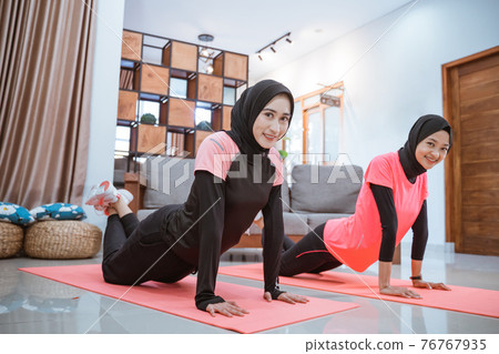 two women wearing hijab sportswear smile while doing push ups together on a mat 76767935