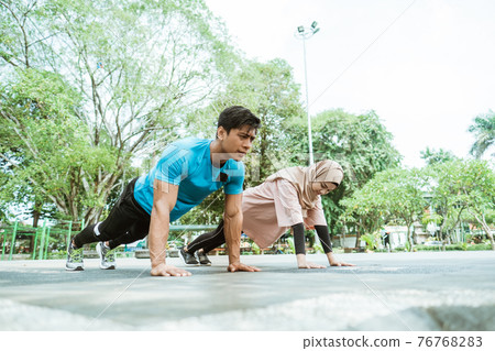 a young man and a girl in a headscarf doing movement to train chest muscles together when outdoor exercise a young man and a girl in a headscarf doing movement to train chest muscles together when outdoor exercise 76768283