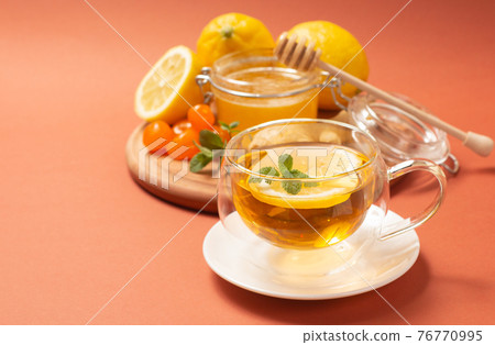 Ginger tea with mint and lemon. Healthy and hot drink. Liquid honey in honey-jar. Crystal cup on bright background. Selective focus. Ginger tea with mint and lemon. Healthy and hot drink. Liquid honey in honey-jar. Crystal cup on bright background. Selective focus. 76770995