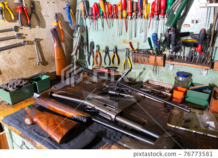 Workplace of gunsmith in weapons workshop with tools and disassembled shotgun 76773581