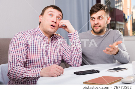 Friend calming distressed guy at home table Friend calming distressed guy at home table 76773592