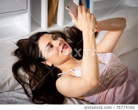 Young sexy woman lying and using phone on white sheet 76774160