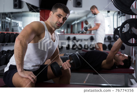 Man doing exercises with dumbbells at gym Man doing exercises with dumbbells at gym 76774356