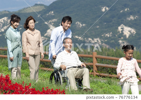 Senior man sitting in a wheelchair and a smiling family Senior man sitting in a wheelchair and a smiling family 76776134