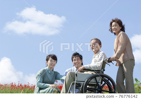 Senior man sitting in a wheelchair and a smiling family Senior man sitting in a wheelchair and a smiling family 76776142