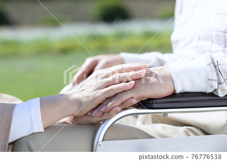 握著一個坐在輪椅上的男人的手的女人 76776538