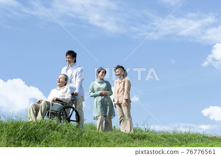 Senior man sitting in a wheelchair and a smiling family 76776561