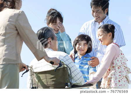 Senior man sitting in a wheelchair and a smiling family 76776569