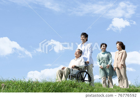 Senior man sitting in a wheelchair and a smiling family 76776592