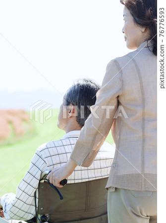 Senior couple walking in a wheelchair 76776593