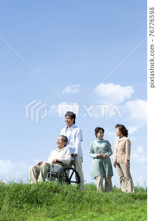 Senior man sitting in a wheelchair and a smiling family 76776598
