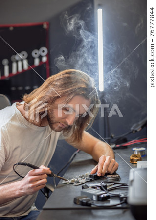 Interested man touching microcircuit with soldering iron Interested man touching microcircuit with soldering iron 76777844