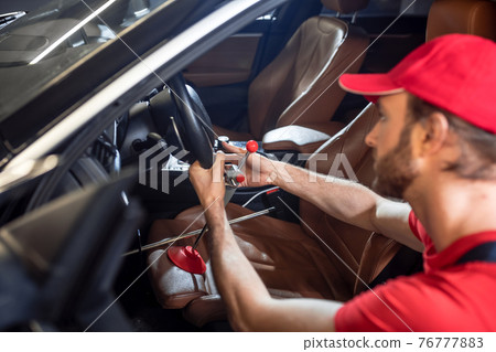 Man holding steering wheel crouched near car Man holding steering wheel crouched near car 76777883