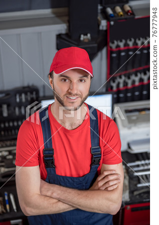 Joyful man in overalls and cap in workshop Joyful man in overalls and cap in workshop 76777948