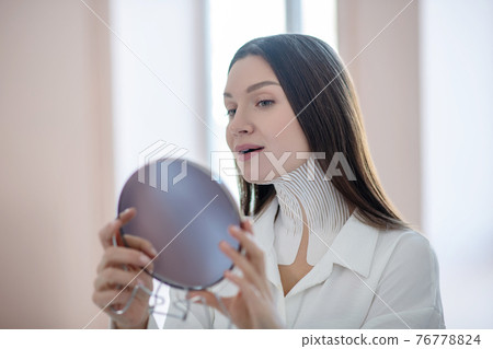 Cute young woman with tapes on her neck looking in the mirror 76778824