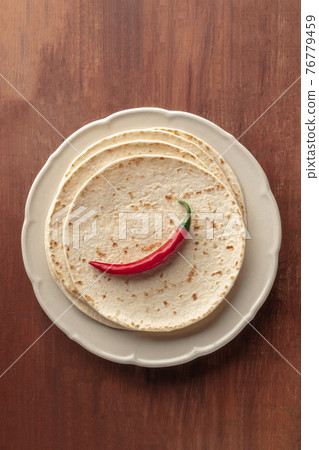 A chili pepper, shot from the top on a pile of tortillas, Mexican flatbreads, on a dark rustic wooden background A chili pepper, shot from the top on a pile of tortillas, Mexican flatbreads, on a dark rustic wooden background 76779459