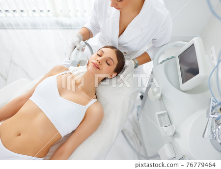 Cosmetologist treating face of woman with laser machine 76779464