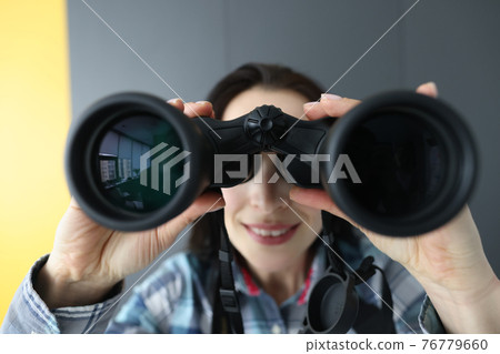 Woman looking through black binoculars and holding it with her hands Woman looking through black binoculars and holding it with her hands 76779660