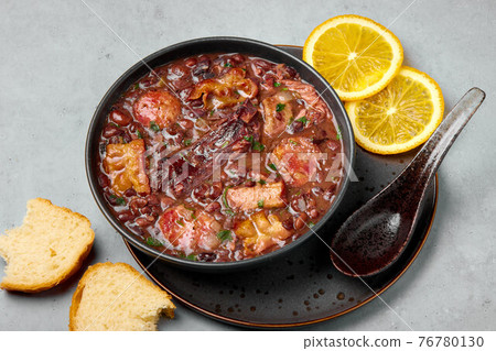 Feijoada in black bowl gray concrete table top. Brazilian and portuguese cuisines beans meat stew Feijoada in black bowl gray concrete table top. Brazilian and portuguese cuisines beans meat stew 76780130