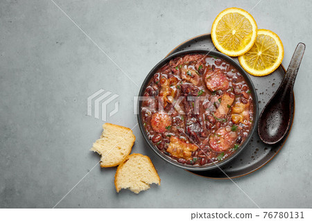 Feijoada in black bowl gray concrete table top. Brazilian and portuguese cuisines beans meat stew 76780131