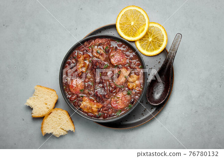 Feijoada in black bowl gray concrete table top. Brazilian and portuguese cuisines beans meat stew Feijoada in black bowl gray concrete table top. Brazilian and portuguese cuisines beans meat stew 76780132
