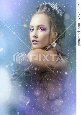 The Snow Queen. Winter girl in a fur coat showered with snow. Model with beautiful makeup on a snowy background. The Snow Queen. Winter girl in a fur coat showered with snow. Model with beautiful makeup on a snowy background. 76780986