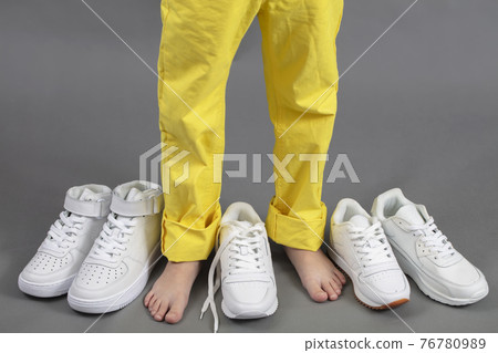 Barefoot on the background of shoes. Feet in a pile of shoes. Children's foot on the background of sneakers. Foot and shoes Barefoot on the background of shoes. Feet in a pile of shoes. Children's foot on the background of sneakers. Foot and shoes 76780989