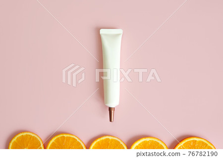 Top view of face and eye cream squeeze, natural cosmetic tube with long nozzle and bronze screw cap and orange slices on pink background. Mockup, template. Skincare and beauty concept 76782190